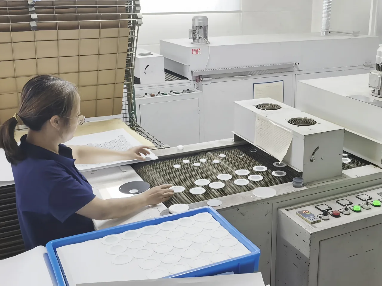 Operator handling circular glass components on a controlled conveyor line.