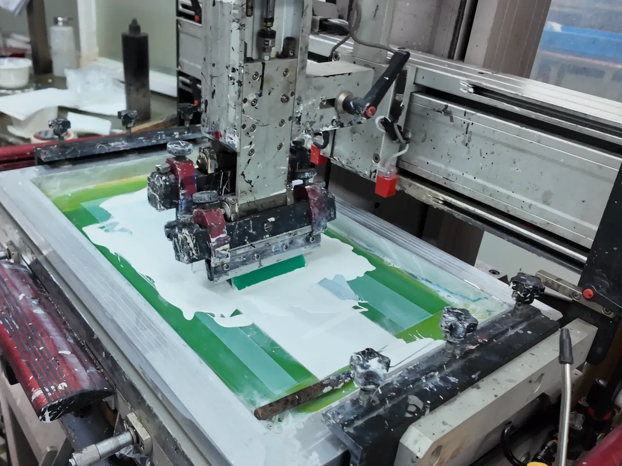 Automatic screen-printing press transferring white ink through a production screen.