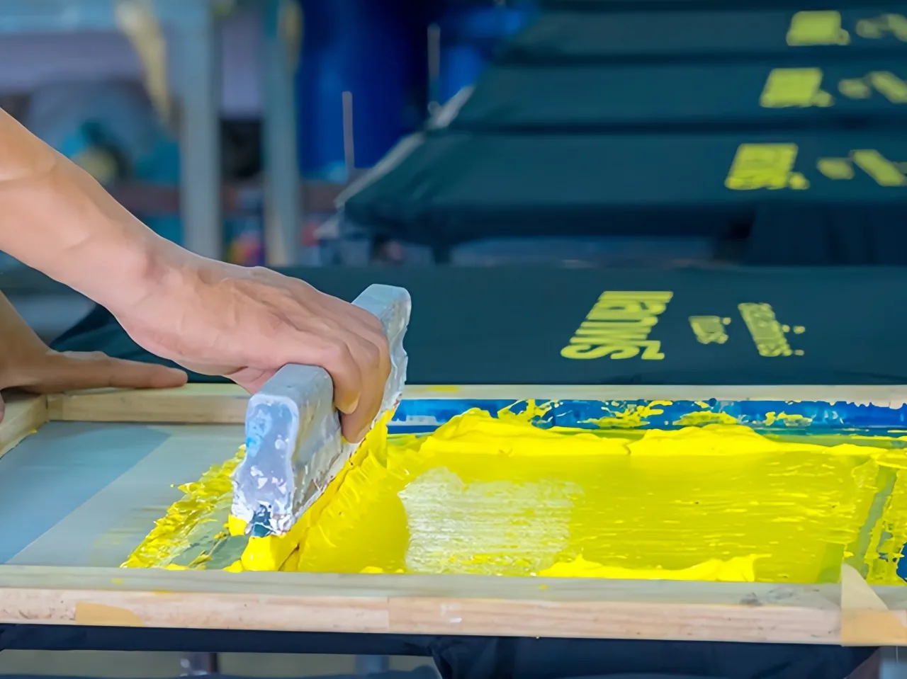 Manual squeegee stroke spreading yellow ink across a screen.