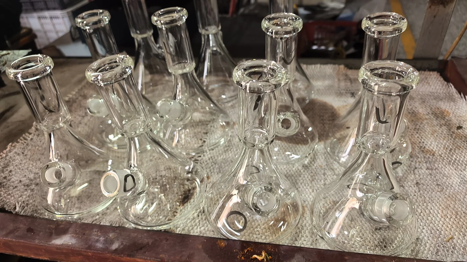 Clear glass vessels with wide neck rims and side openings on a fabric-covered workbench.