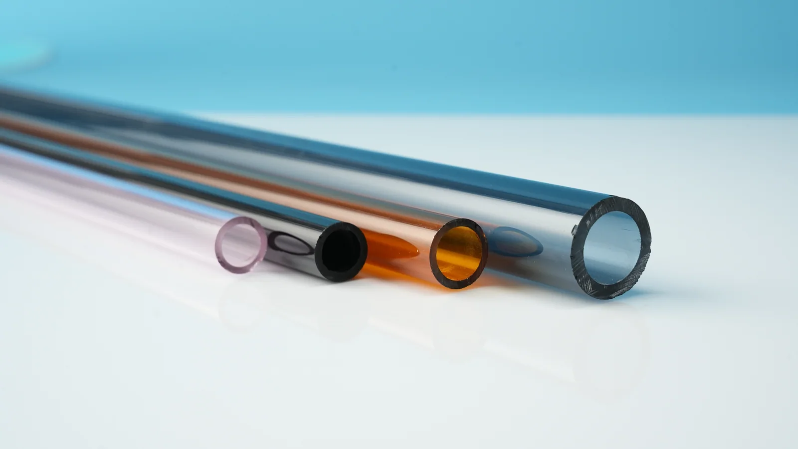 Four coloured hollow glass tubes with their cut ends visible, in pink, dark, amber and blue-grey tones.
