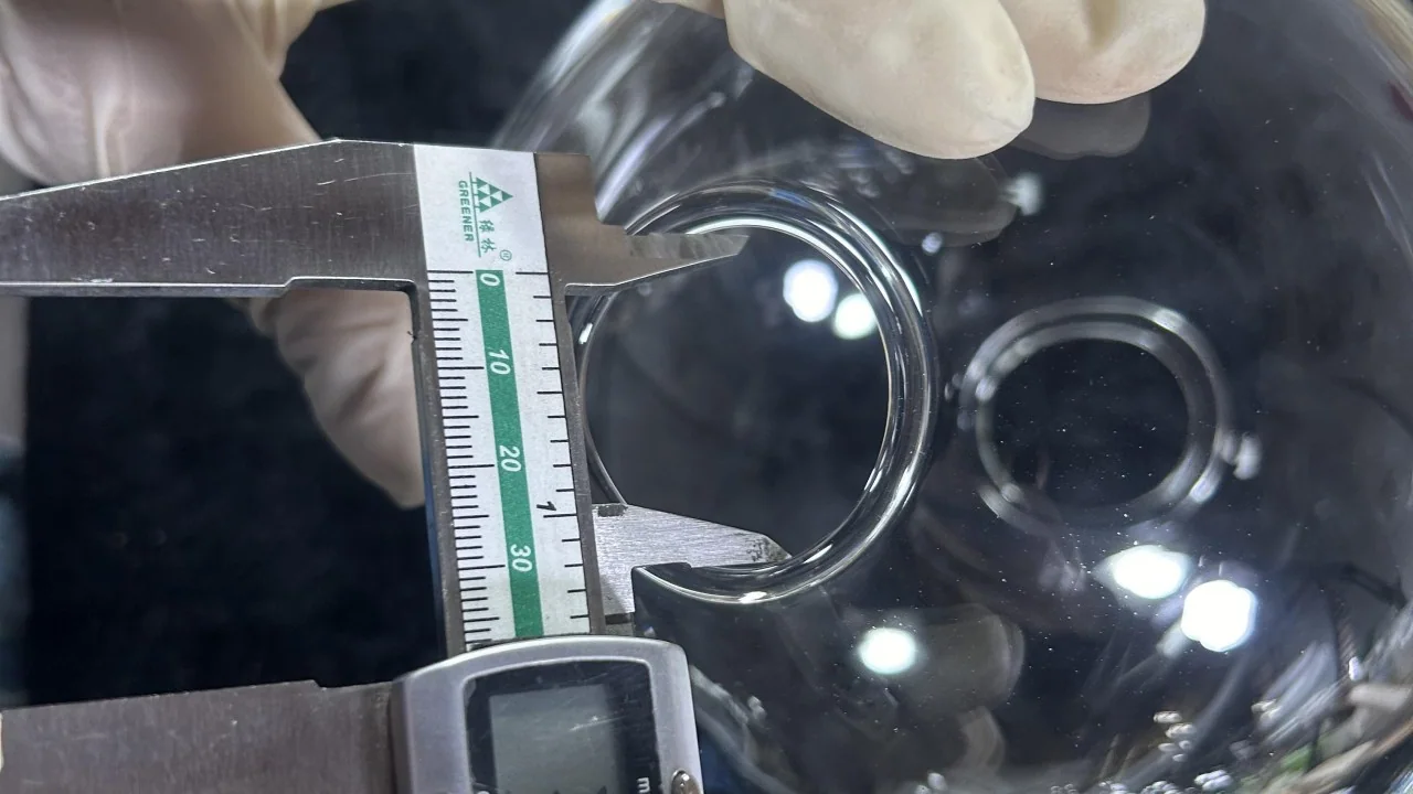 Gloved hands using the inside jaws of a digital calliper to check the opening of a formed glass part.