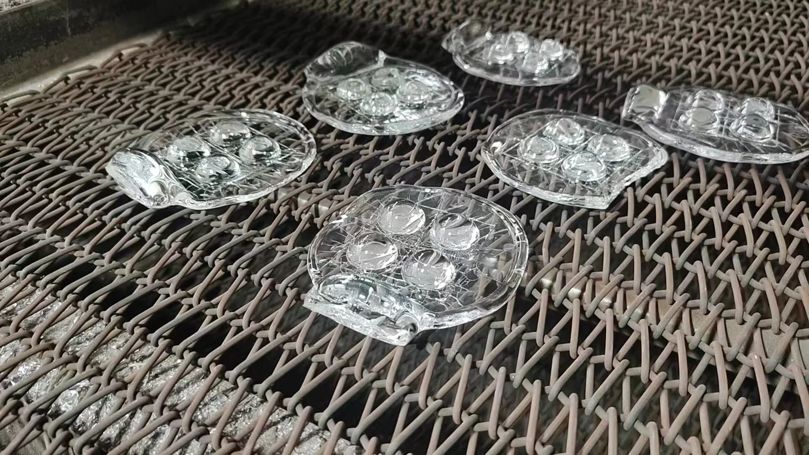 Clear formed glass components moving along a metal mesh conveyor