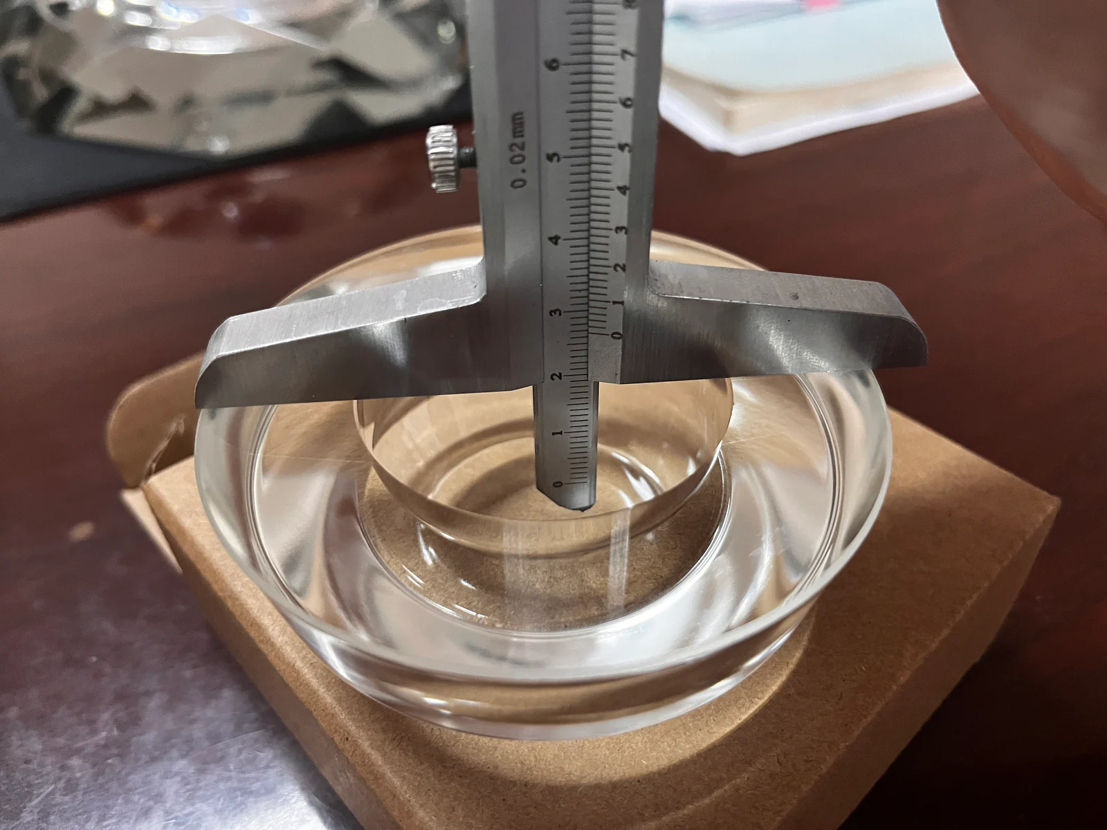A vernier depth gauge positioned across the rim of a clear glass component for a dimensional check