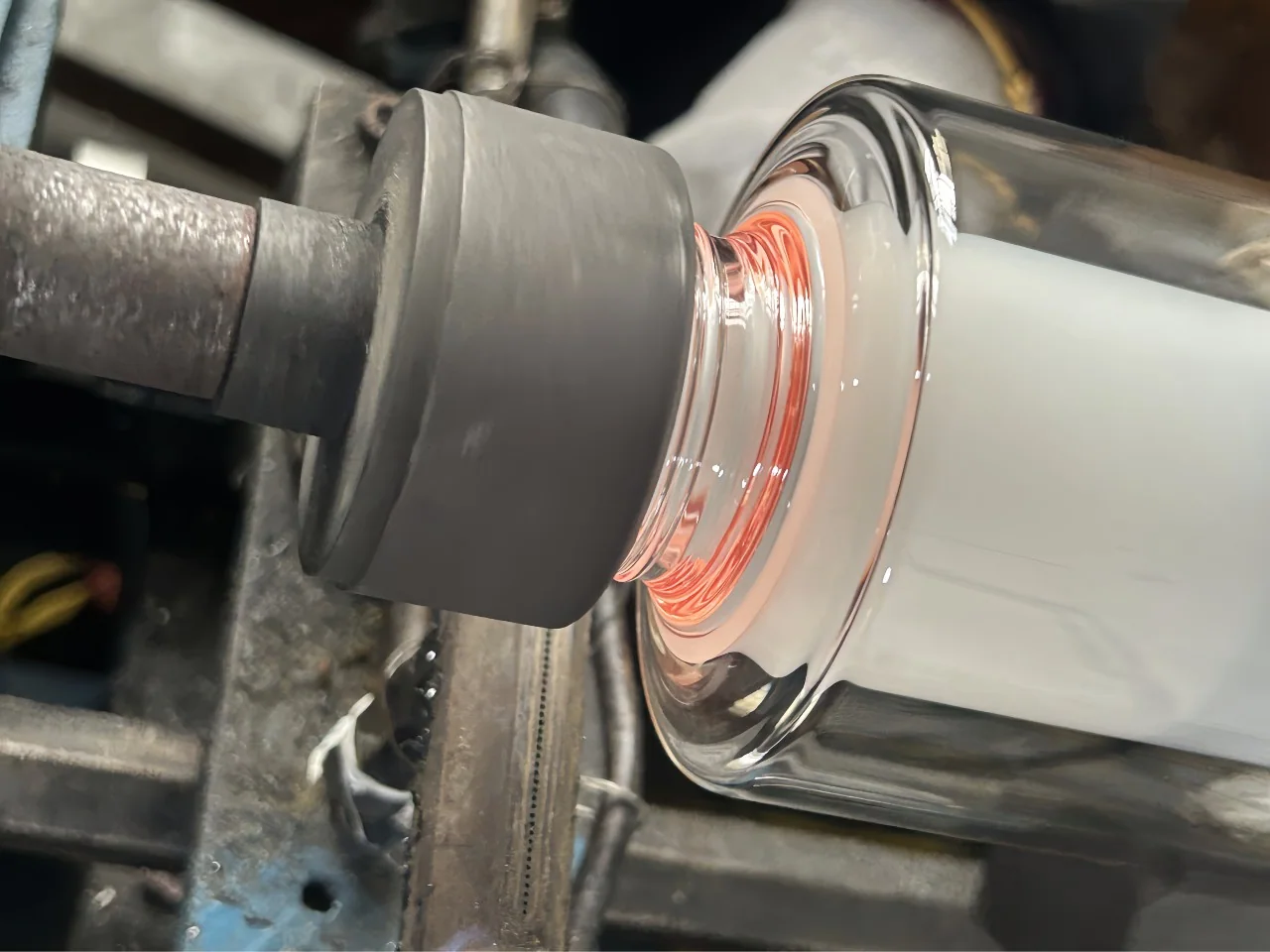 A cylindrical tool positioned at the neck of a clear glass component.