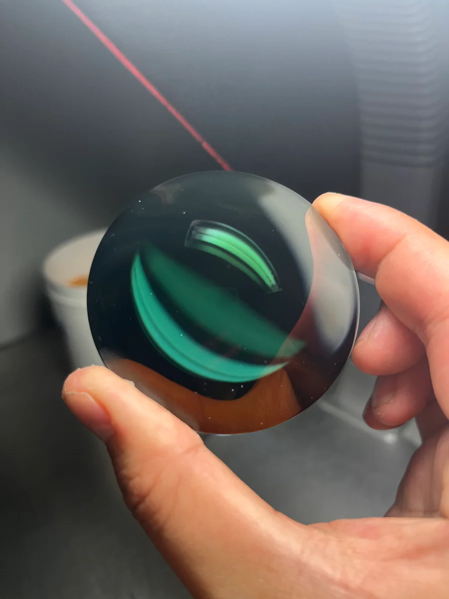 Hand-held circular glass component showing green and dark coloured reflections