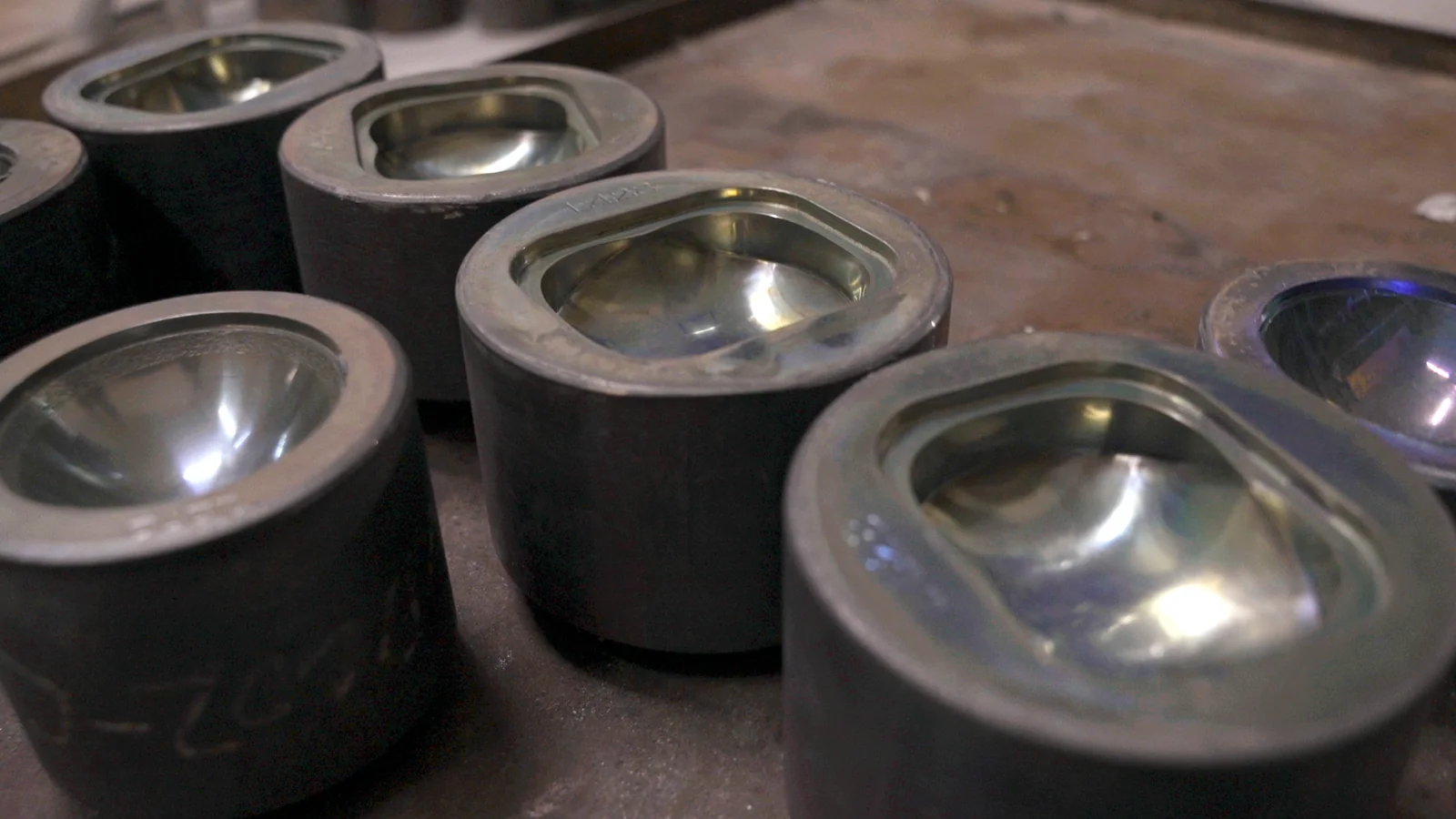 Several glass pressing tools with polished curved cavities on a workshop bench