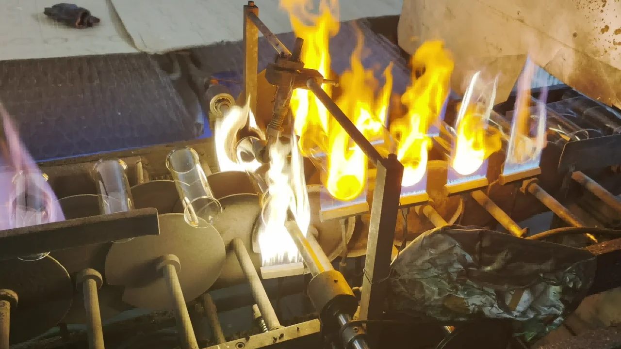 Several clear glass tubes positioned among mechanical wheels and local burners on a forming station.