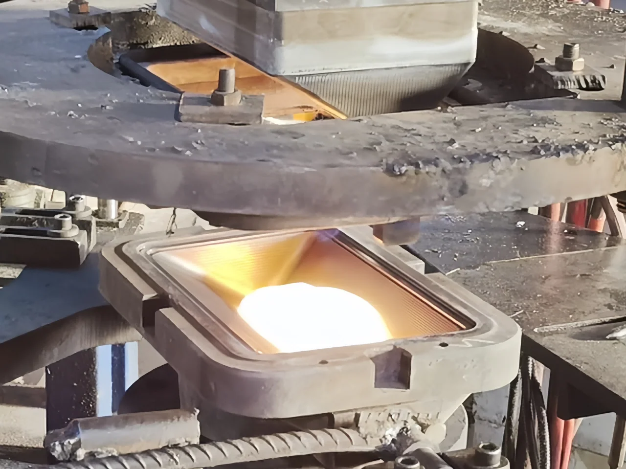 A molten glass charge in a rectangular mould beneath a raised patterned press plunger