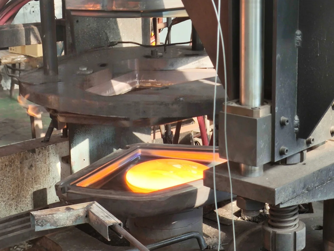 An orange molten-glass charge resting in a rectangular mould beneath a raised press plunger