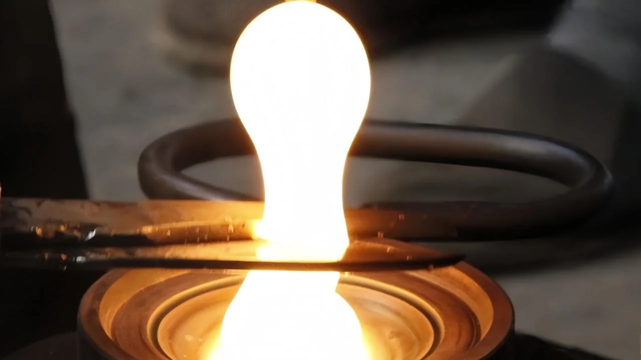 A glowing molten glass gather being sheared above a round mould