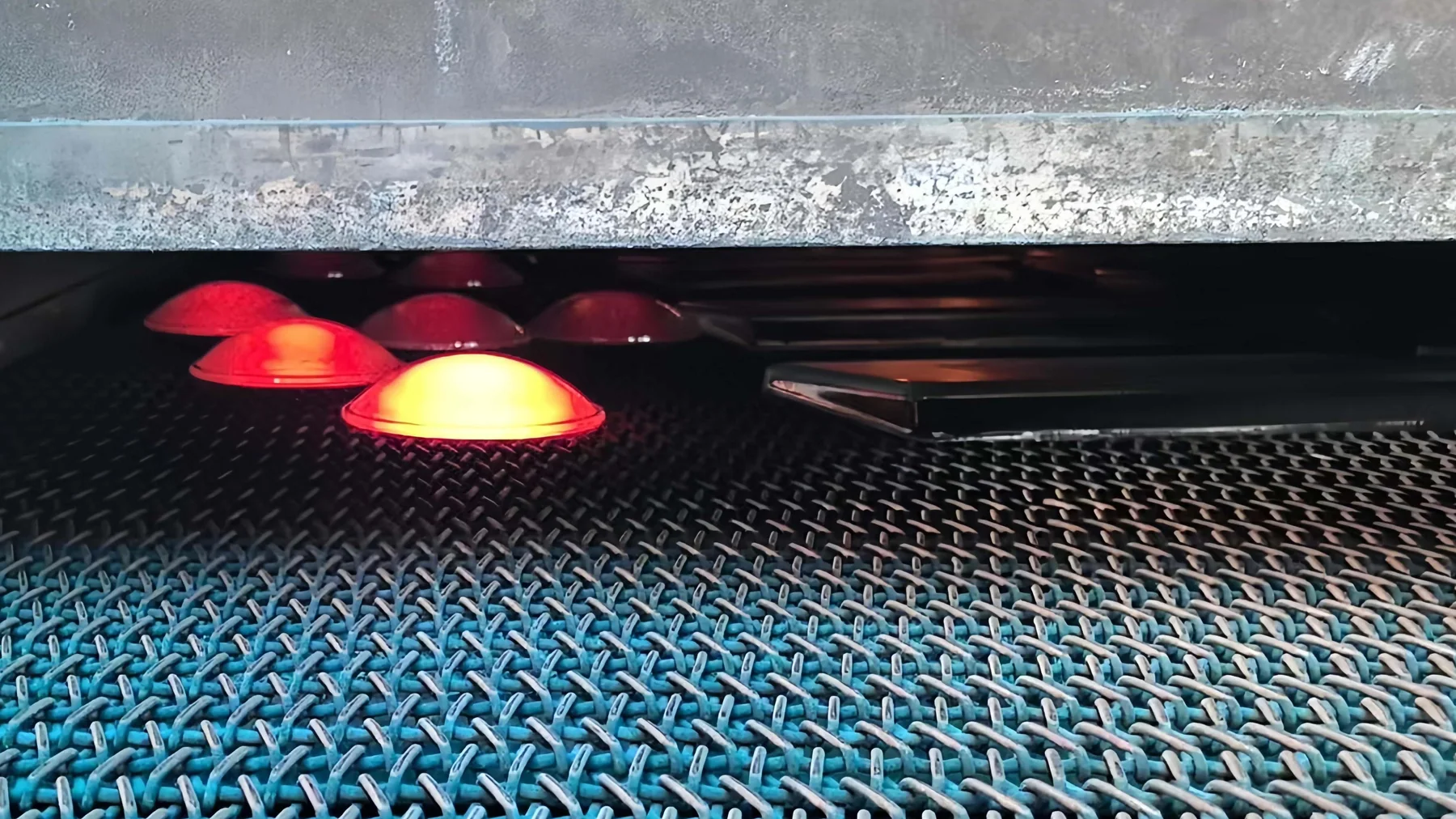 Hot dome-shaped and rectangular glass components on a conveyor at an annealing lehr