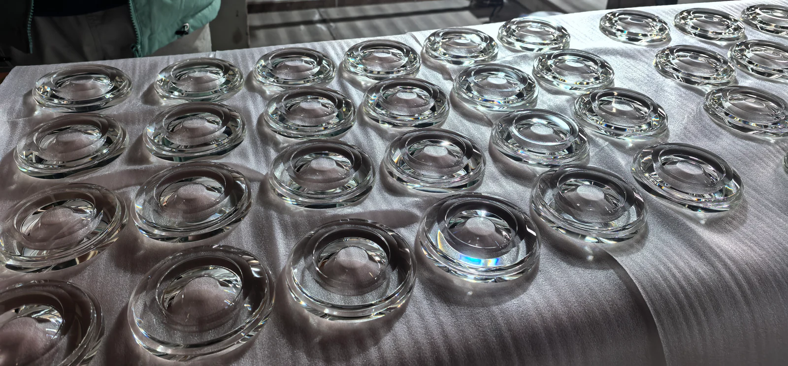 Rows of clear circular glass components with curved faces arranged on a light-coloured work surface