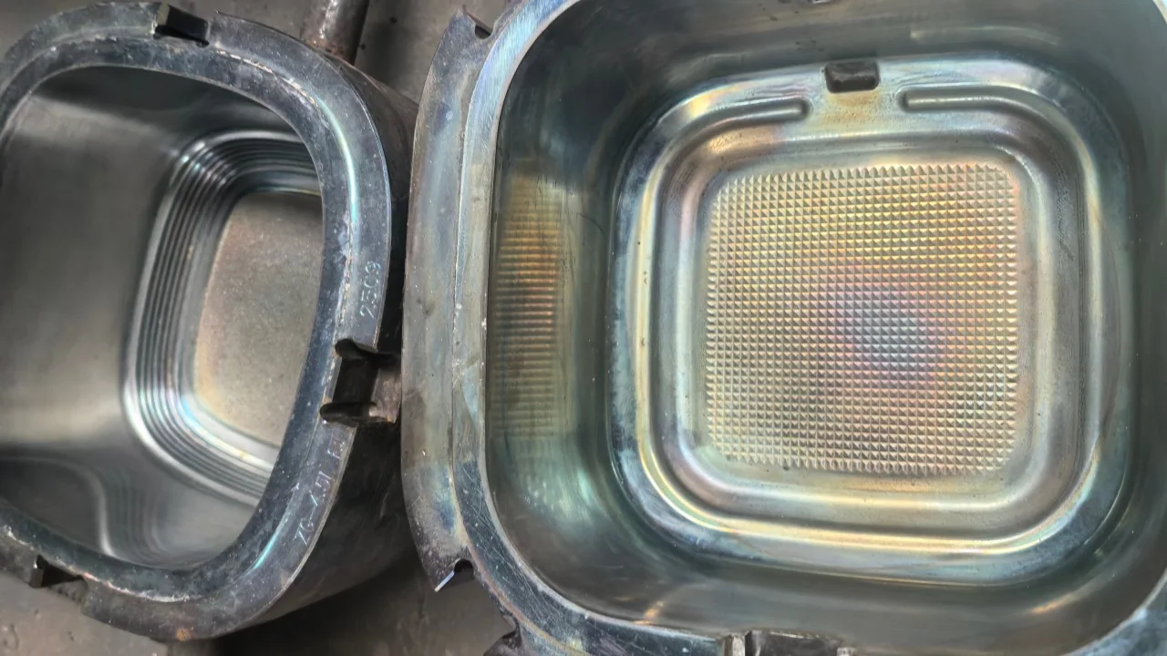Metal pressing cavity with rounded rectangular contours and a patterned central area, beside a separate ring.