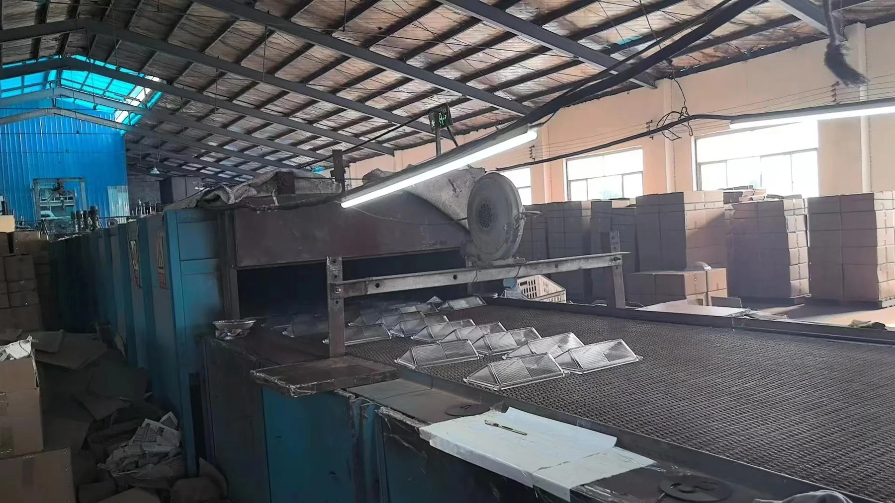 Rectangular pressed-glass covers spaced on a mesh conveyor at an annealing lehr