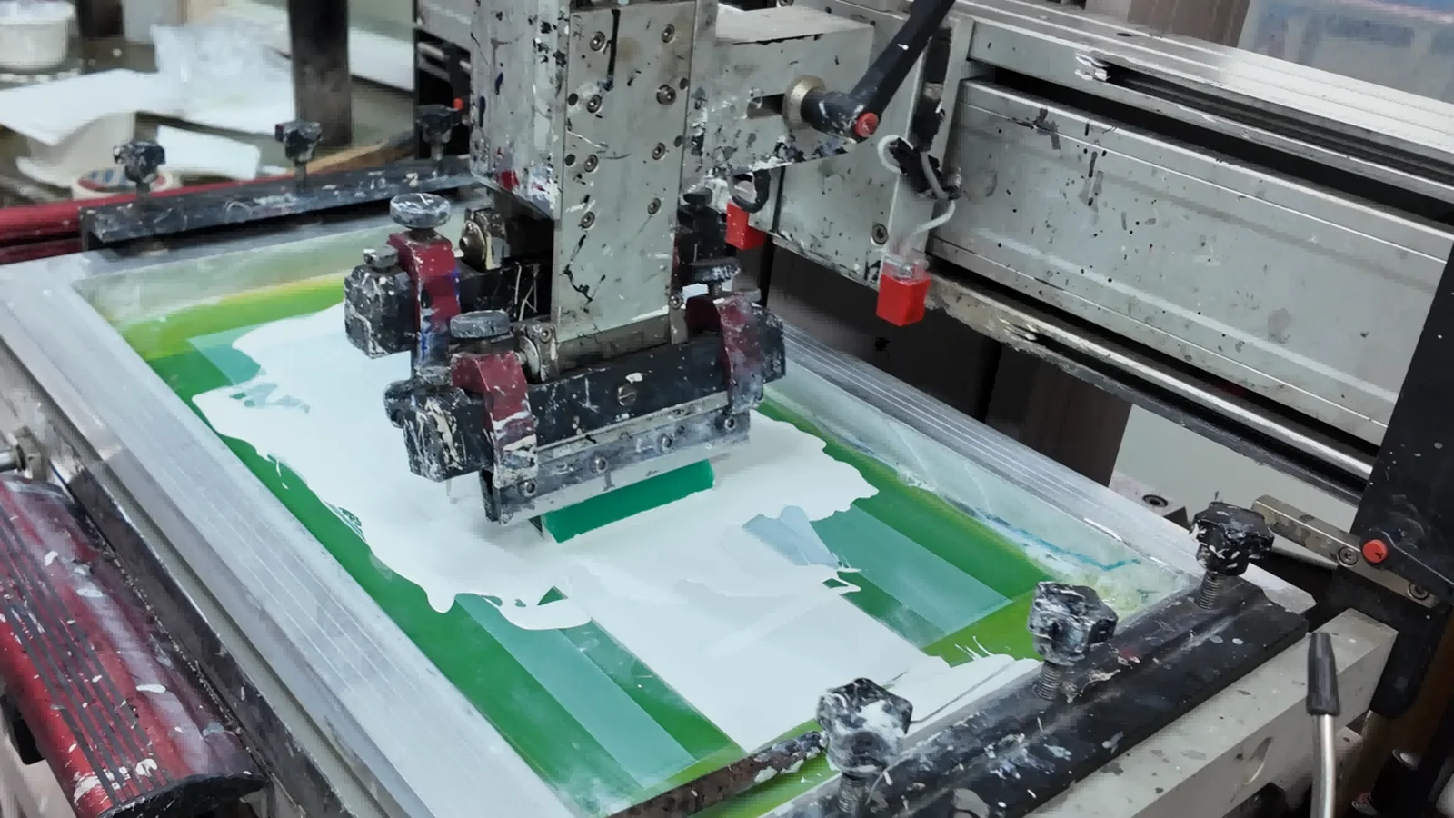 Real factory screen-printing press transferring white ink through a production screen.