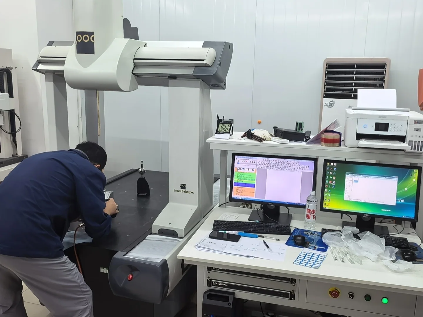Operator using a coordinate measuring machine beside two computer displays
