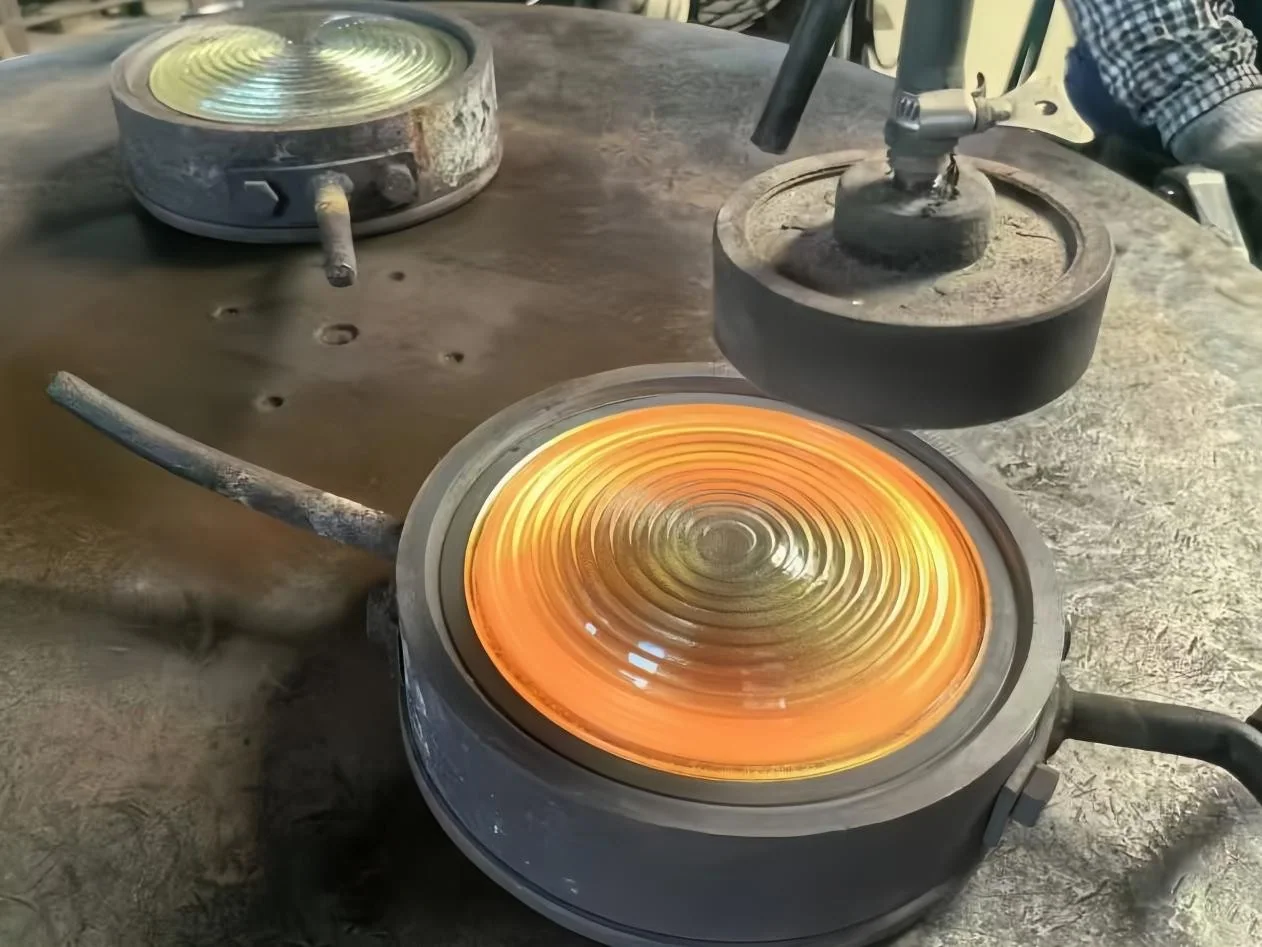 A hot concentric-ribbed glass article supported in an open round mould beside the withdrawn forming tool