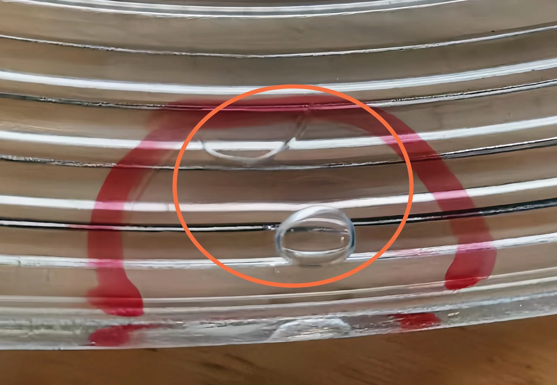 Close-up of ribbed clear glass with an orange circle around rounded and elongated visible features.