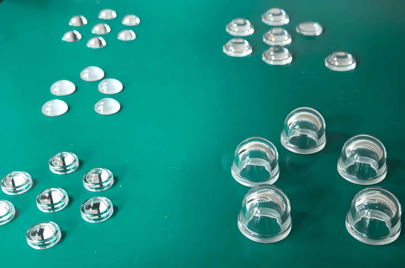 Groups of small clear glass components with domed and flanged profiles on a green display surface